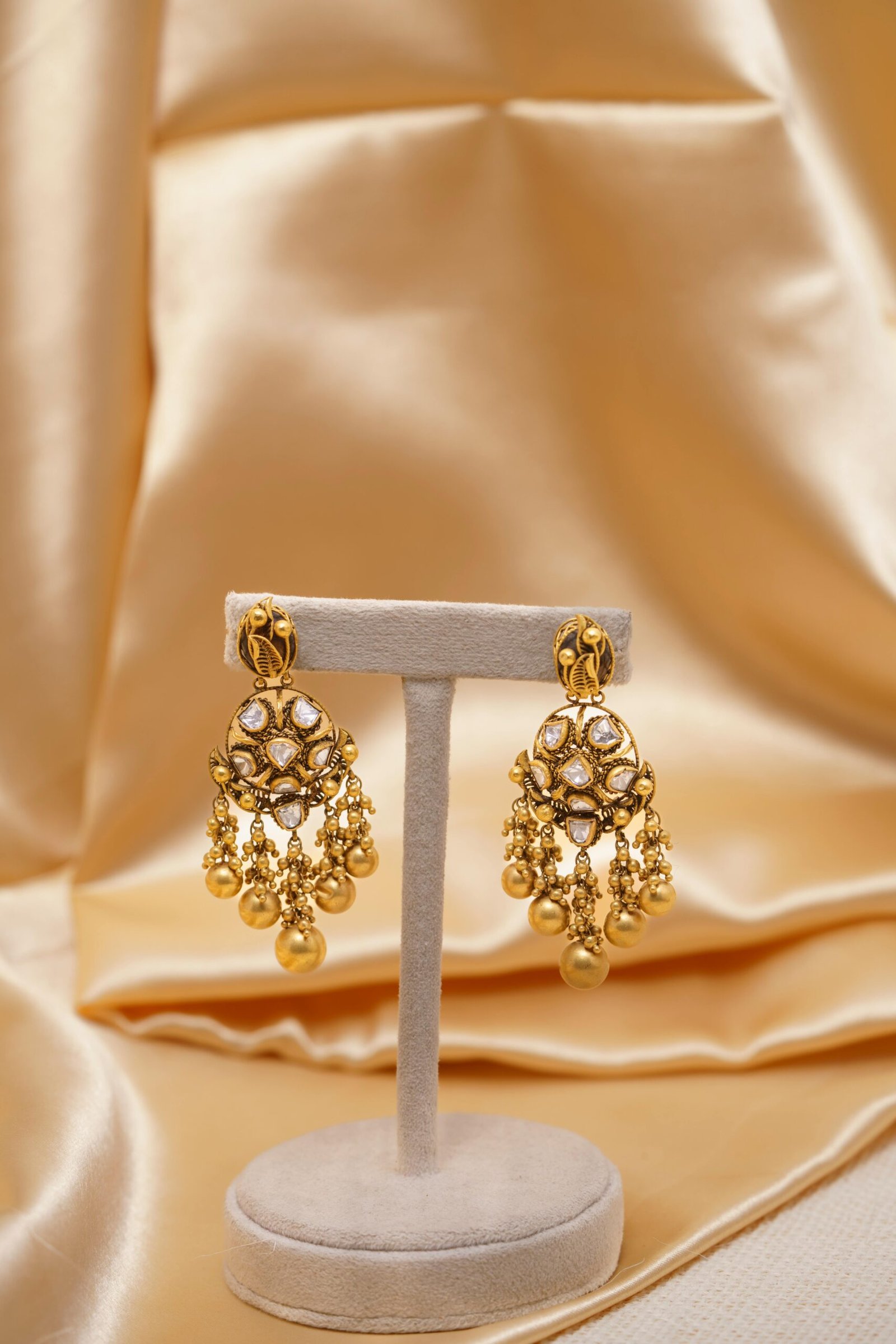 Elegant gold chandelier earrings displayed on luxurious gold satin backdrop. Perfect for formal occasions.